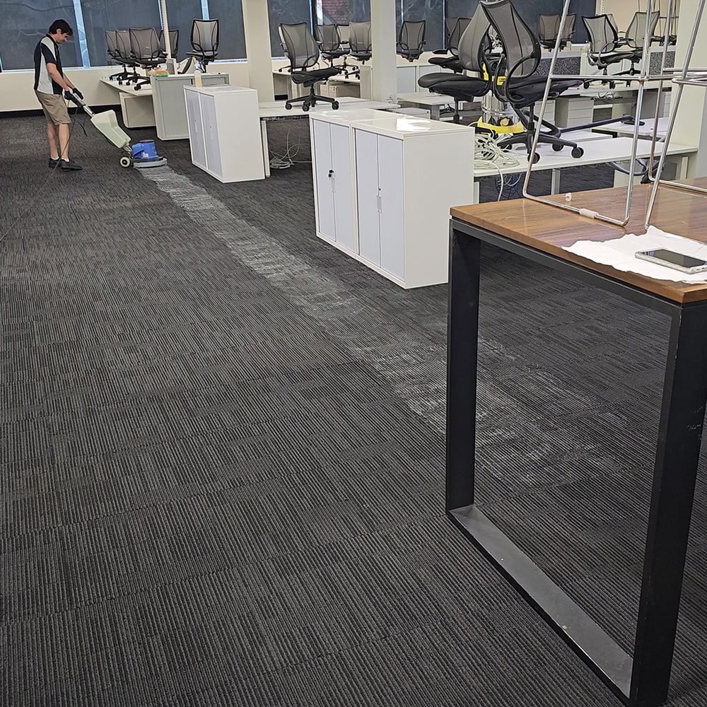 Commercial carpet cleaner at work in a Perth open-plan office, one of our own technicians cleaning the carpet tiles between desks.
